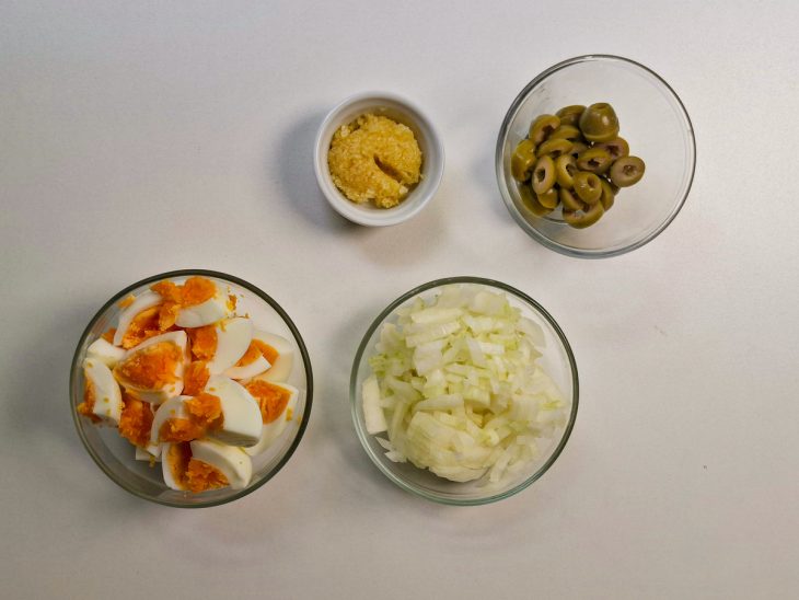 Alho, cebola, ovos e azeitonas picados e separados em recipientes distintos.