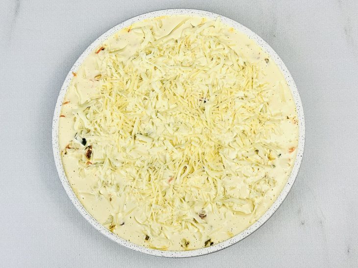 Camadas de recheio, massa e queijo parmesão ralado adicionados a forma.