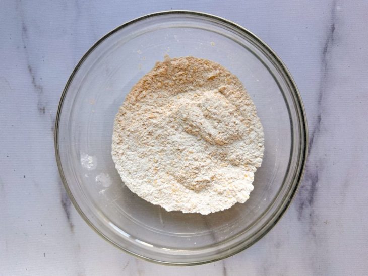 Farinhas, fermento e sal misturados numa tigela redonda de vidro.