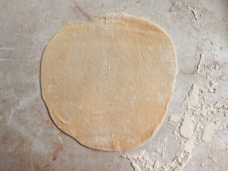 Discos finos sendo abertos em bancada enfarinhada.