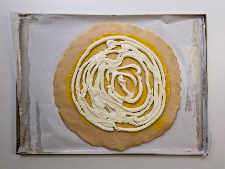 Camada de mostarda e queijo sendo espalhada sobre a base da massa.