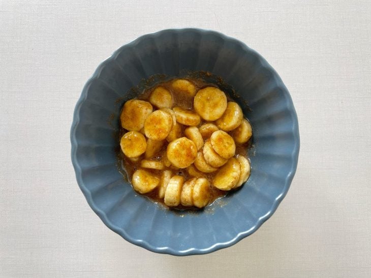 Rodelas de banana sendo misturadas com suco de limão, açúcar e canela em um bowl.