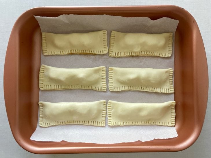 Bordas das tortinhas sendo pressionadas com os dentes de um garfo para selar.