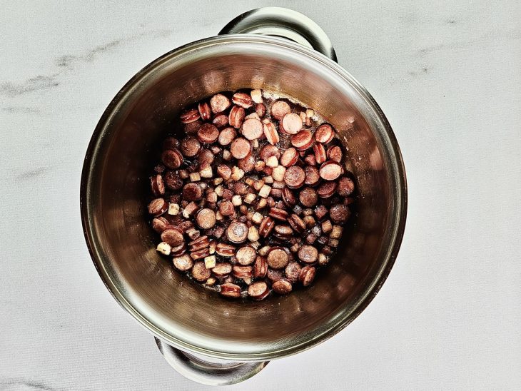 Bacon e linguiça fininha adicionados em uma panela para fritar.