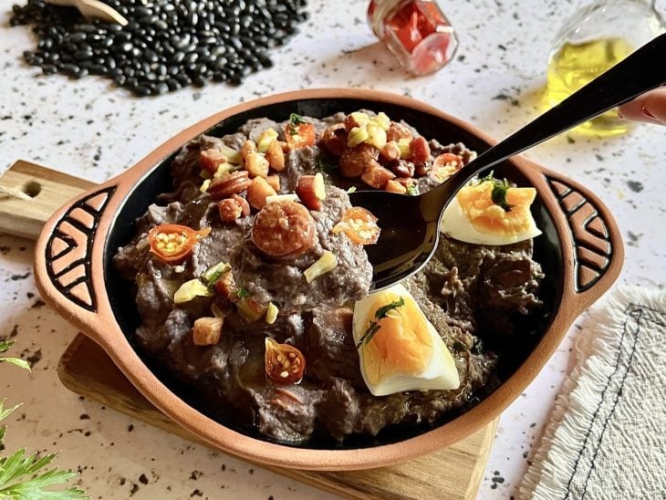 Tutu de feijão-preto finalizado com ovos, refogado de linguiça e bacon, cheiro-verde e pimenta biquinho, pronto para consumo.
