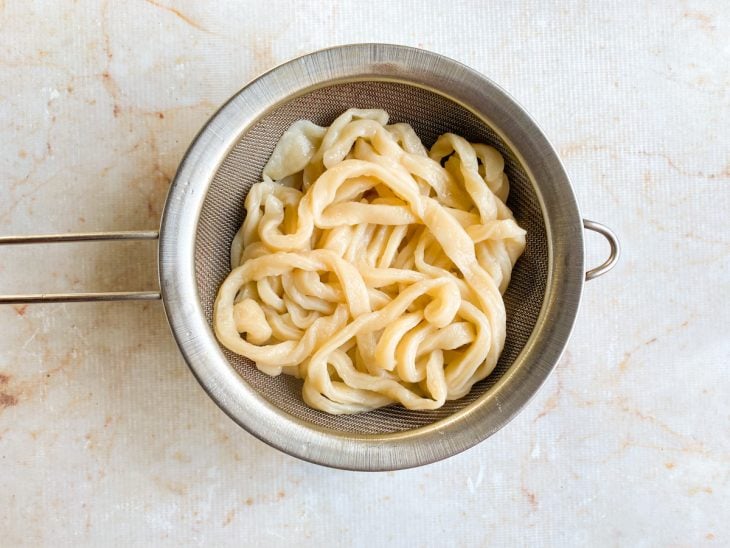 Uma peneira sobre a tigela com o udon escorrido.