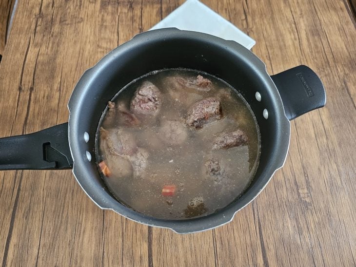 Panela com costelas e temperos cobertos por água.