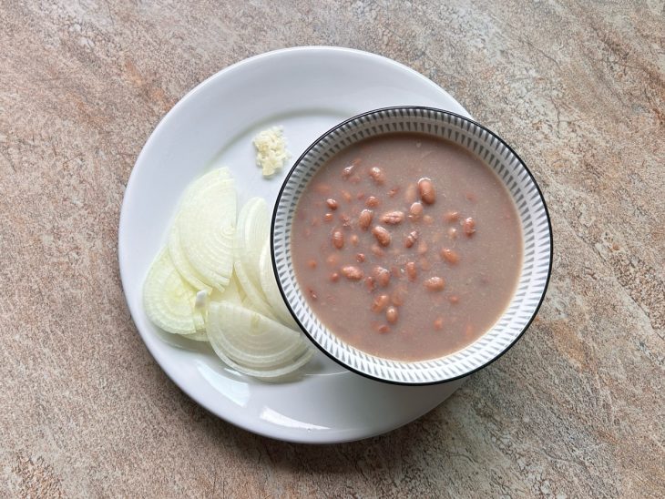 Prato com cebola e alho cortados e tigela com feijão já pronto.