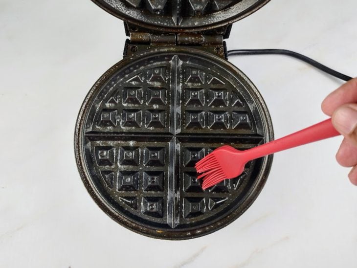 Máquina de waffle sendo pincelada com azeite.