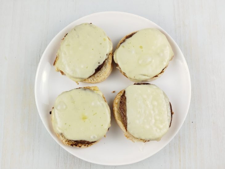 Hambúrgueres com queijo derretido acomodados sobre as fatias de pão num prato.