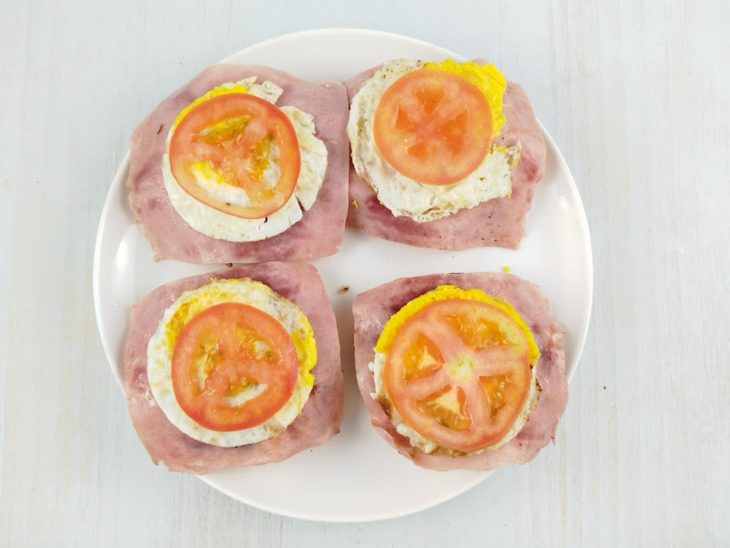 Fatia de presunto, ovo e tomate acomodados sobre o hambúrguer.