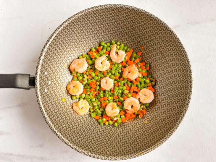 Camarões e legumes fritando na panela.