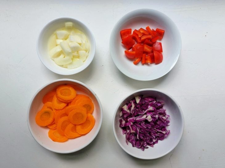 Repolho, cenoura, pimentão e cebola cortados e separados em potinhos.